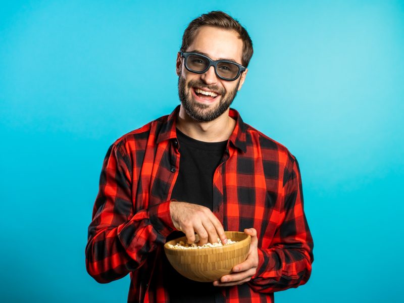 manl-in-3d-glasses-watching-fascinating-comedy-movie-laughing-and-eating-popcorn-on-blue-studio.jpg